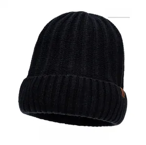 Detail of black knit beanie featuring vertical ribbed texture and brown leather logo patch