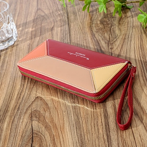 Detail of color-block patchwork women long wallet with zipper and wrist strap on wood