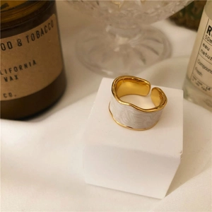 Close-up of golden irregular wave ring with white enamel on a minimalist pedestal