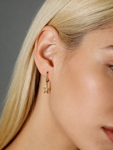 Close-up of a model wearing a gold starfish pendant charm on a small hoop earring