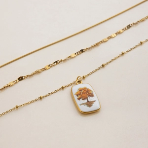 Détail d'un collier multicouche plaqué or 18k avec un pendentif arbre en émail