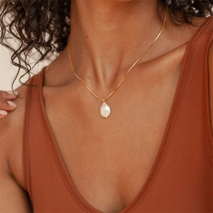 Collier élégant en plaqué or avec pendentif en perle baroque blanche porté par un mannequin