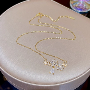 Detail of gold floral necklace with teardrop crystal pendant on textured cushion