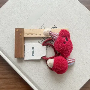 Detail of red plush hair ties featuring plaid cone hat accents and embroidery