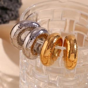 Textured 18K gold and silver chunky C-shape hoop earrings on a decorative glass