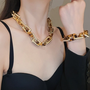 Dettaglio di un set collana e bracciale a maglie quadrate in metallo dorato e acrilico