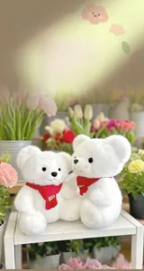 Close-up of two plush white teddy bears with red scarves in a field of tulips