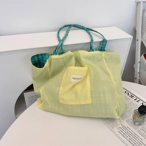 Detail of a bright yellow canvas tote bag featuring green checkered lining and outer pocket
