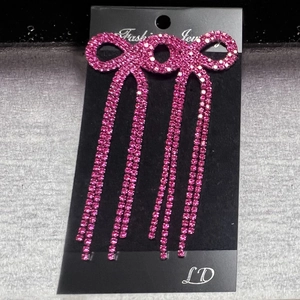 Detailed view of pink rhinestone bow earrings with tassels on a black jewelry card
