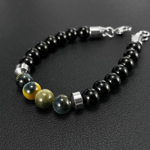 Detail of beaded bracelet with black, yellow, and green tiger eye stones on textured surface