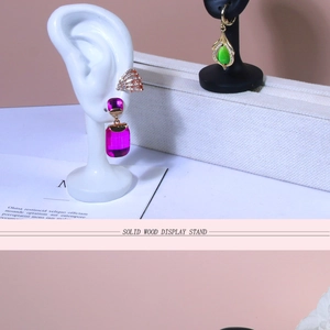 Detail view of ear display stand with purple and green gemstone earrings on white ear model