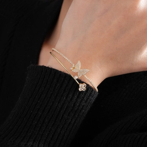 Detail of gold double-layer bracelet with zircon butterfly and clover on model's wrist