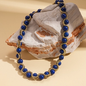 Dettaglio di perline in pietra blu scuro intrecciate con catena dorata su roccia naturale