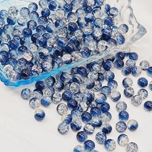 Detail of 6mm-8mm blue crackle glass beads spilling from a bowl onto white fabric