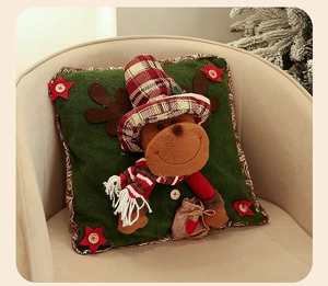 Detail of velvet Christmas pillow with 3D reindeer design and red plaid hat on sofa