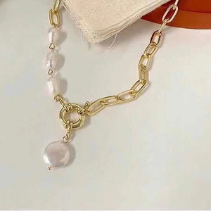 Close-up of golden paperclip chain and white pearl necklace with large sailor clasp