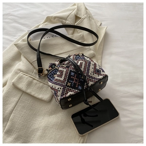 Detail of a woven geometric bucket bag with black leather drawstring on a beige blazer