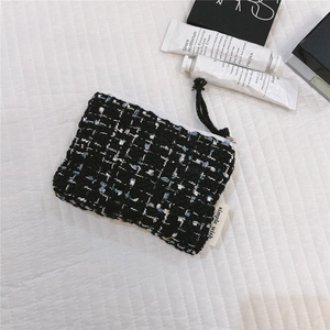 Detail of tweed coin purse with white zipper and tassel on a quilted white surface