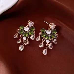 Elegant gold drop earrings with green petals and white zircon tassels on silk background