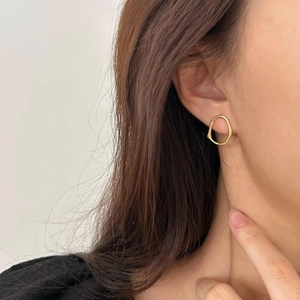 Close-up of a model wearing irregular gold-plated geometric oval earrings with a polished finish