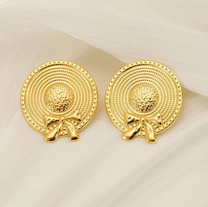Macro detail of golden straw hat earrings with bowknot on white silk background