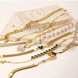 Detailed flat lay of assorted gold-plated chain bracelets with pearls and charms on stone