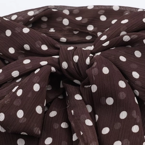 Detail of a dark brown bow tie with white polka dots on lightweight chiffon fabric