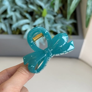 Detailed view of glossy cyan bow-shaped hair claw clip with strong gold metal spring