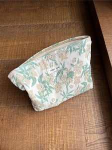 Nahaufnahme der floralen Baumwoll-Kosmetiktasche mit grünem Blattmuster auf Holzgrund