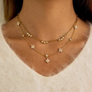 Detail of layered gold clover necklace with paperclip chain and zircon on a model