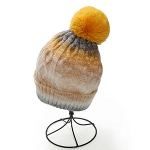 Detail showing gradient cable knit texture and yellow faux fur pompom on winter hat