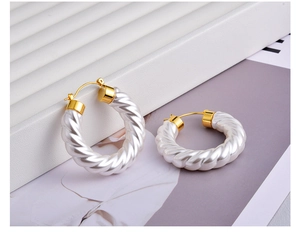 Detail of twisted white resin hoop earrings with golden metal clasps on a display tray