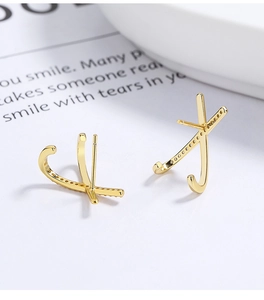 Close-up of golden X-shaped sterling silver stud earrings with sparkling pavé crystals