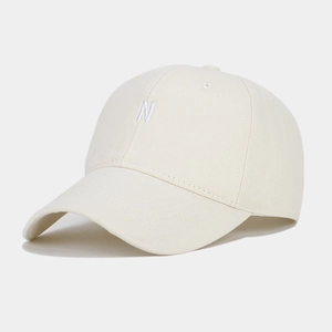 Detail of embroidered white N letter on cream cotton baseball cap with ventilation eyelets