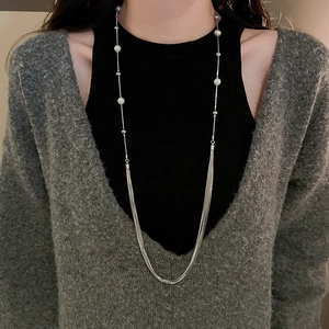Detail of silver multi-layer long pearl necklace draped on a grey knit cardigan
