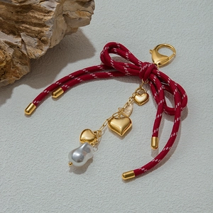 Golden keychain with red woven bow, baroque pearl, and heart charms on a stone backdrop