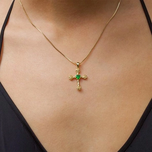 Détail macro du pendentif croix en or avec zircon cœur vert et relief rose sur chaîne