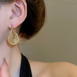 Close-up of golden multi-layer twisted teardrop earring worn by a model in soft light