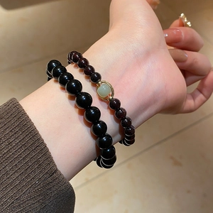 Detail of obsidian and garnet beaded bracelet set with gold hollow charm on model wrist