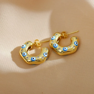 Detailed close-up of golden C-shaped earrings with blue evil eye enamel and micro zircons