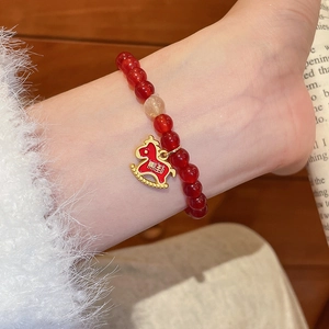 Gros plan d'un bracelet en perles d'agate rouge avec un pendentif cheval doré gravé