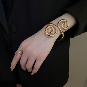 Close-up of polished gold spiral cuff bracelet and matching ring on model in black blazer