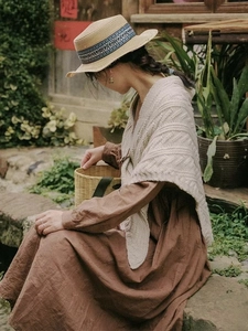 Detail of beige knit shawl paired with a vintage brown dress and straw hat in a garden