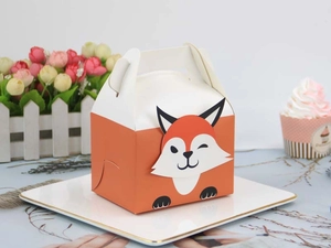Detail of fox-shaped cardboard baking box with handle on white plate for pastry gift