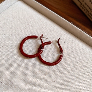 Macro shot of deep red circular hoop earrings with a glossy finish and silver needles