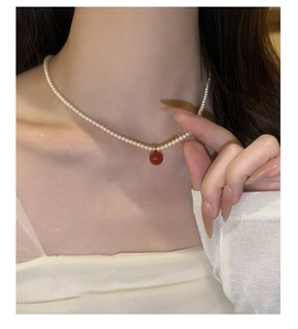 Détail d'un collier de perles avec pendentif sphérique rouge sur le cou d'un mannequin
