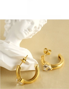 Detailed close-up of C-shaped gold earrings with zircon on a white artistic statue