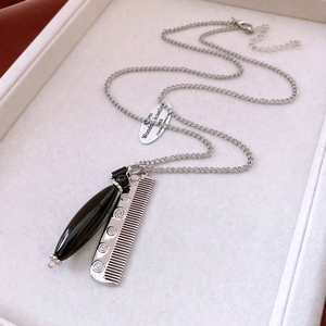 Close-up of vintage silver necklace featuring black teardrop and comb charms with engraving