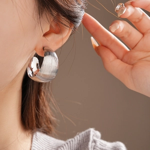 Close-up of silver wide C-shaped hoop earrings with brushed metallic texture on model