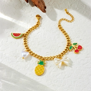 Detailansicht eines goldenen Armbands mit bunten Emaille-Anhängern aus Früchten und Schleifen